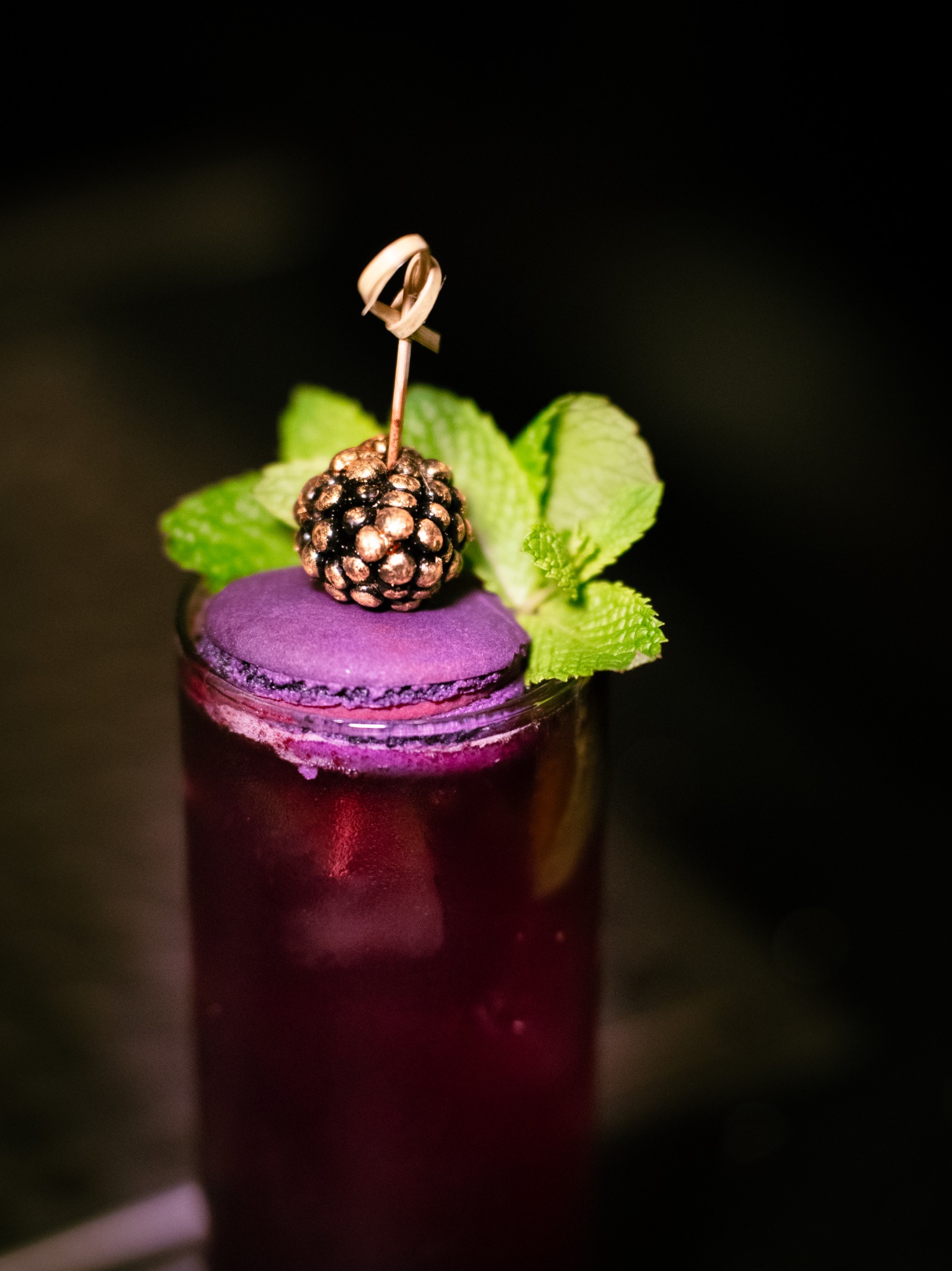 Purple cocktail with a macaron, blackberry, and mint garnish photographed by ShutterQueue