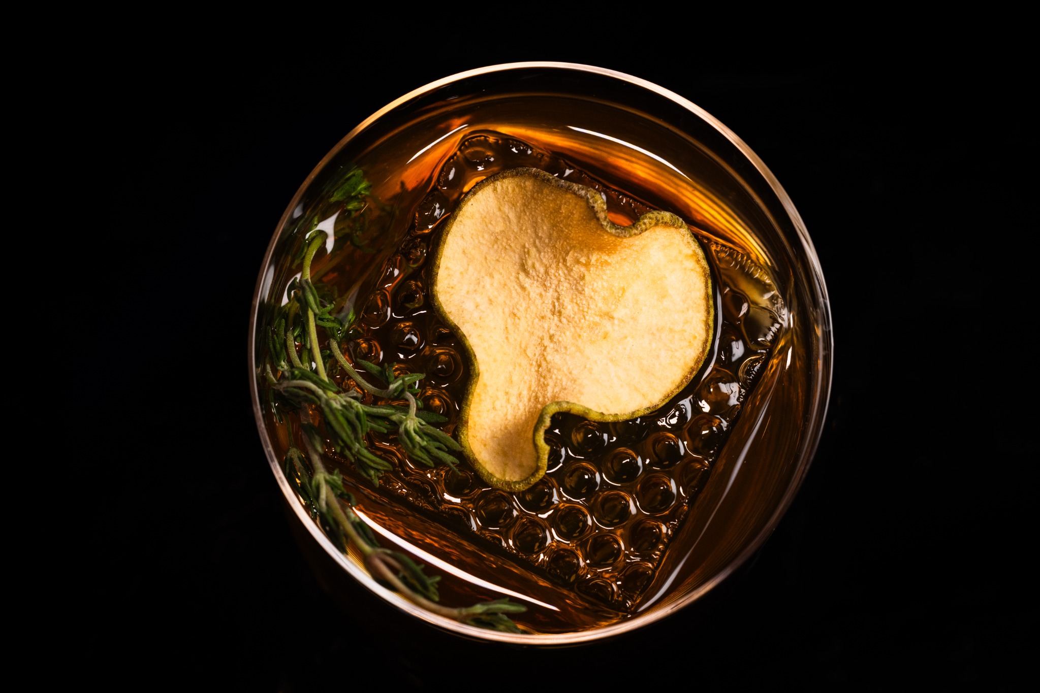 Overhead view of an amber cocktail with a pear-shaped garnish