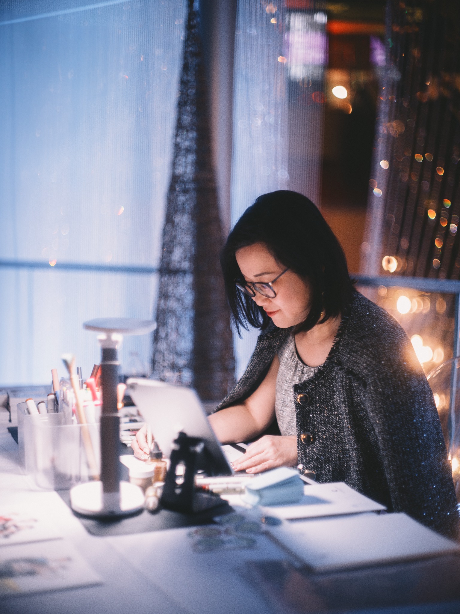 A woman drawing at her desk beside a softly lit window, photographed by ShutterQueue